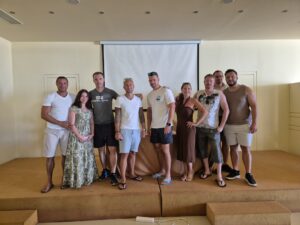 Teamfoto von zehn Personen auf einer kleinen Bühne vor einer Leinwand, alle leger gekleidet.