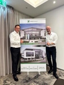 Zwei Männer in Businesskleidung präsentieren stolz ein Roll-Up mit dem Green Business Center Linz.