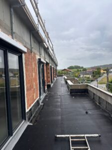 Blick entlang einer noch unvollständig ausgebauten Dachterrasse mit Baugerüst und Blick auf eine Wohngegend.