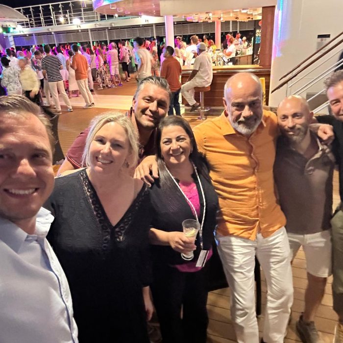 Teamfoto auf dem Deck eines Kreuzfahrtschiffs bei Nacht, umgeben von bunt beleuchteter Tanzfläche.