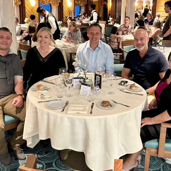 Fünfköpfige Gruppe sitzt gemeinsam elegant gekleidet beim Dinner an einem runden Tisch im Restaurant.