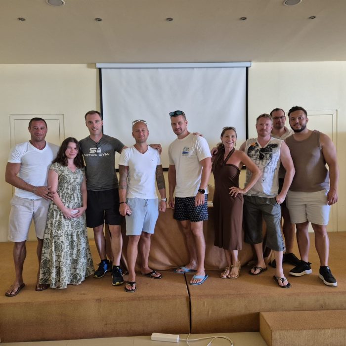 Teamfoto von zehn Personen auf einer kleinen Bühne vor einer Leinwand, alle leger gekleidet.