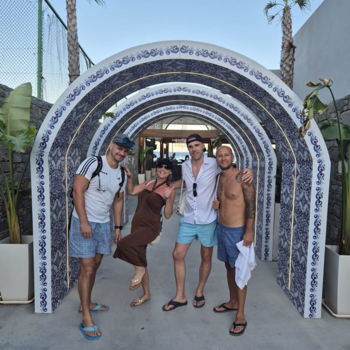 Vier Personen posieren gut gelaunt unter einem kunstvoll gestalteten Torbogen am Eingang eines Resorts.