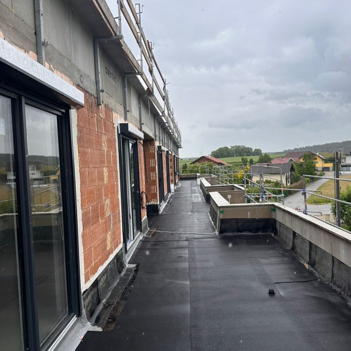 Blick entlang einer noch unvollständig ausgebauten Dachterrasse mit Baugerüst und Blick auf eine Wohngegend.