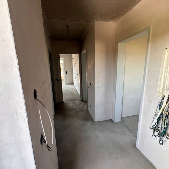 Ein leerer Flur in einem Neubau mit offenen Kabeln und Rohinstallationen an Wänden und Decke.